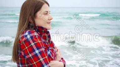 女人看着海滩上的海浪。 女旅行者在暴风雨天气的海滩度假时很冷